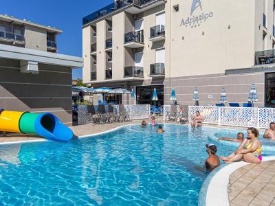 Piscine ensoleillée d'hôtel avec toboggan coloré et gens détendus.
