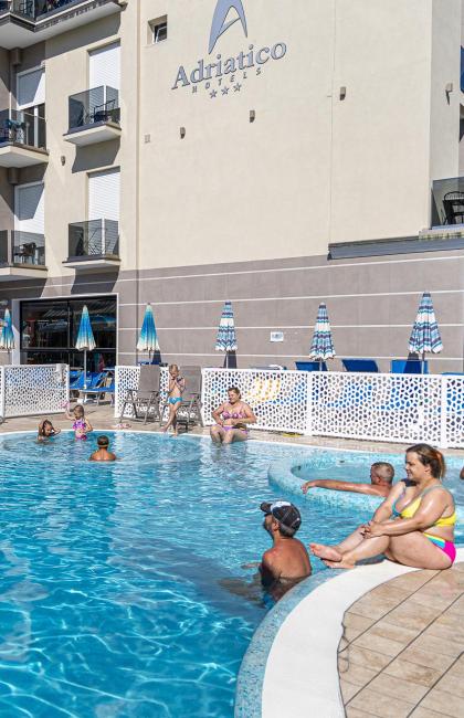 Piscina soleggiata in hotel con scivolo colorato e persone rilassate.