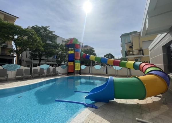 Piscina con scivolo colorato e lettini, situata all'aperto.