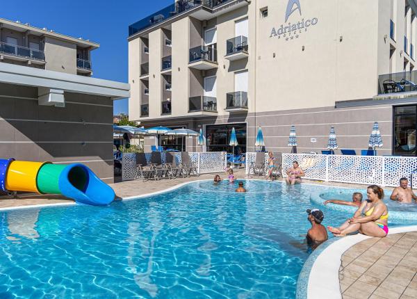 Piscine ensoleillée d'hôtel avec toboggan coloré et gens détendus.