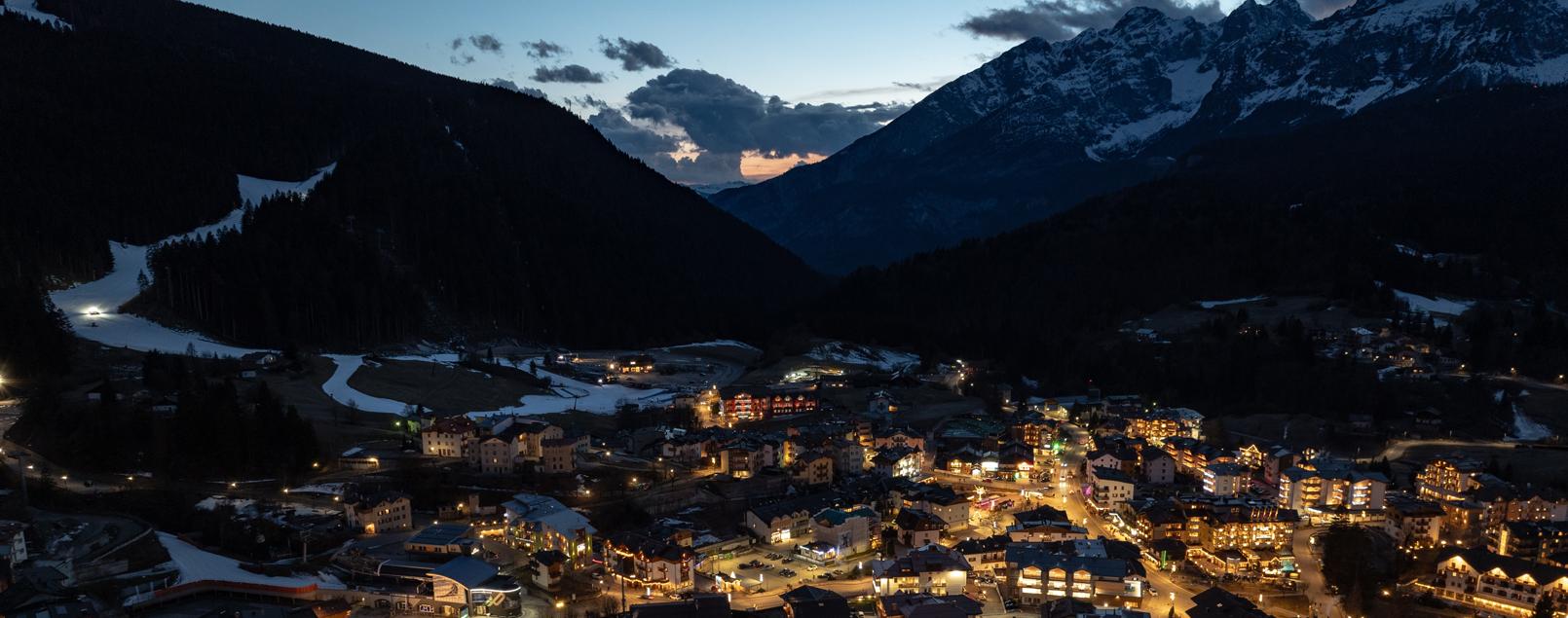 Vista notturna di un villaggio alpino illuminato con montagne sullo sfondo.