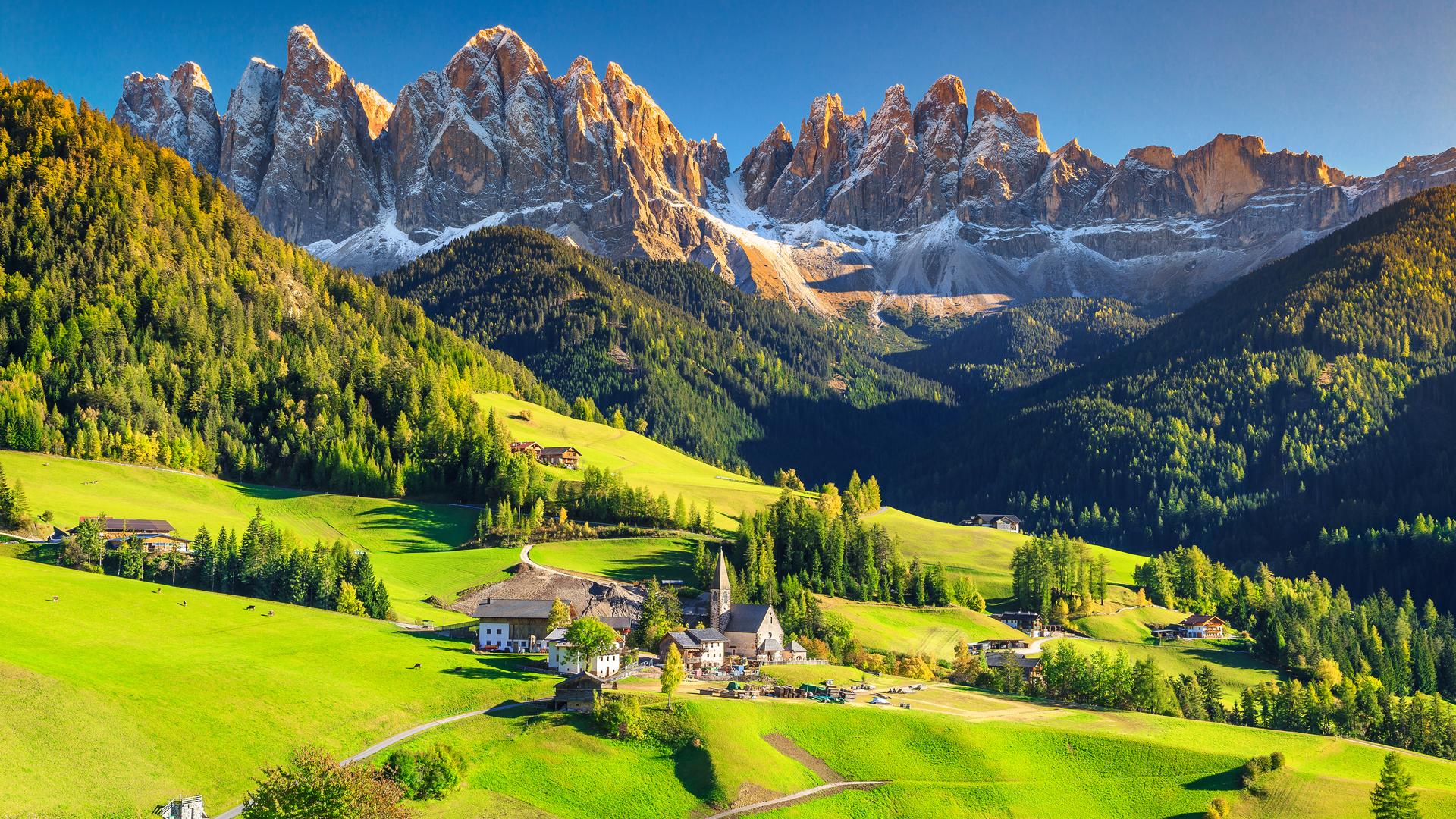 Paesaggio alpino con montagne, prati verdi e un villaggio pittoresco.