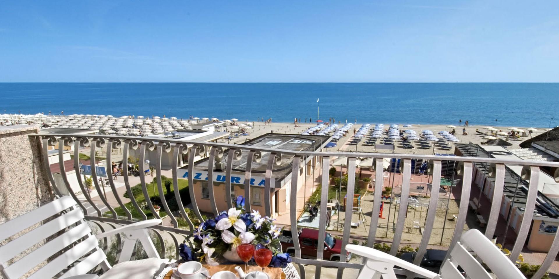 Vue sur la mer avec plage et transats, table avec fleurs et boissons.