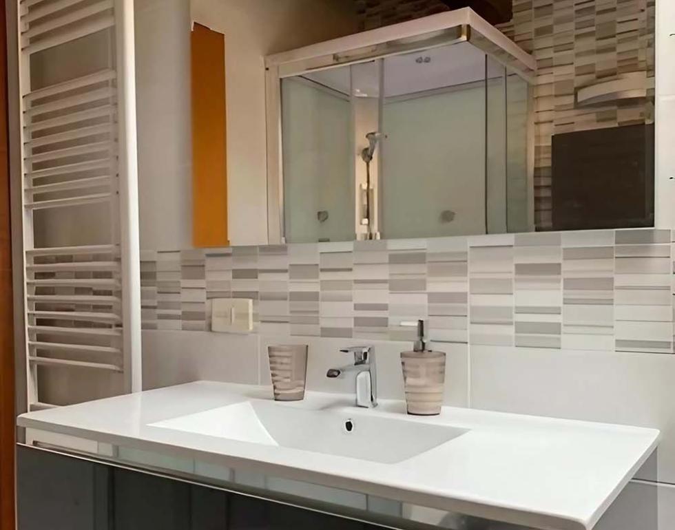 Bagno moderno con lavabo, doccia e specchio, armadio sotto il lavandino.