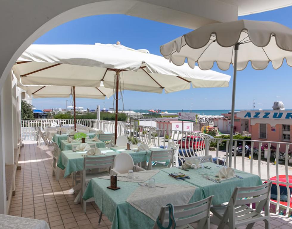 Terrasse avec tables dressées, vue sur la mer, parasols blancs.